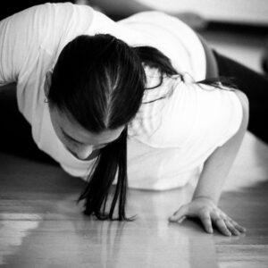 Student in Christine Germain's Class on their stomach on the floor with knees bent, feet tilting towards. on side