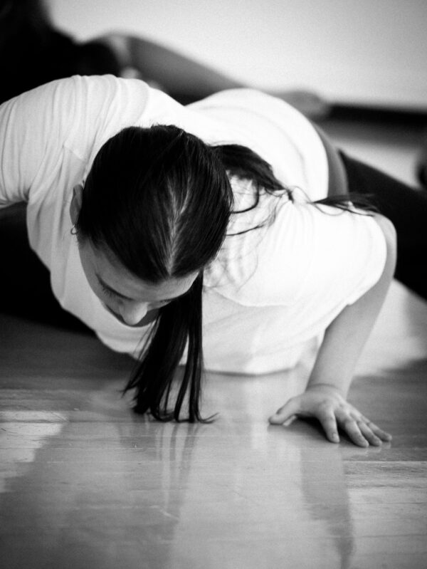 Student in Christine Germain's Class on their stomach on the floor with knees bent, feet tilting towards. on side